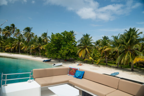 View from the deck of a luxury sailing catamaran in San Blas, Panama, showing crystal-clear water, palm trees, and white sandy beaches.