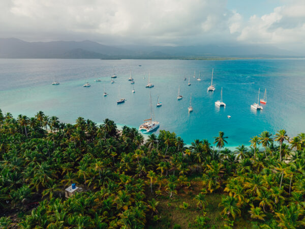 Aerial photo of multiple sailboats anchored off the lush green islands of San Blas, Panama, surrounded by turquoise Caribbean waters.