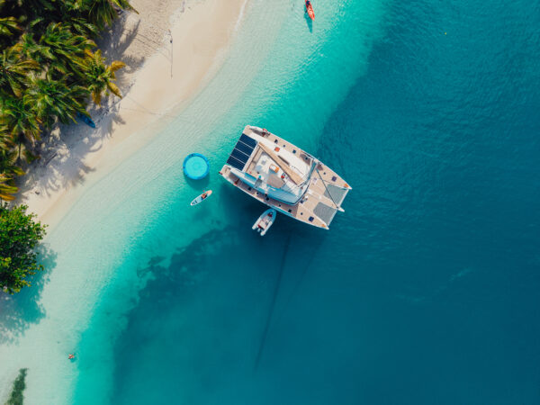 Aerial view of a luxury catamaran anchored near a tropical beach in San Blas, Panama, with clear blue waters and palm trees.