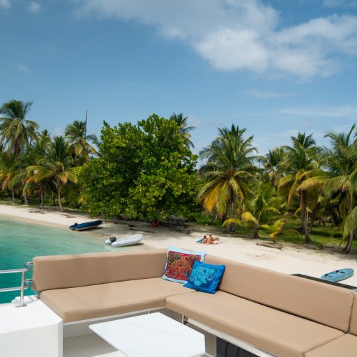 luxury-catamaran-deck-san-blas-panama-tropical-beach-view.jpg View from the deck of a luxury sailing catamaran in San Blas, Panama, showing crystal-clear water, palm trees, and white sandy beaches.