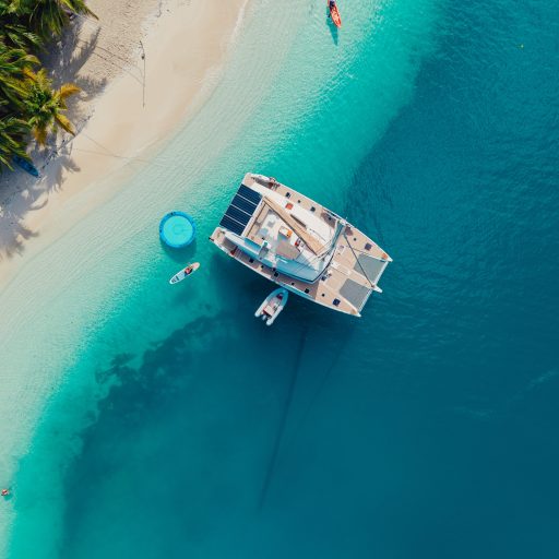 luxury-sailing-catamaran-san-blas-panama-beach Aerial view of a luxury catamaran anchored near a tropical beach in San Blas, Panama, with clear blue waters and palm trees.